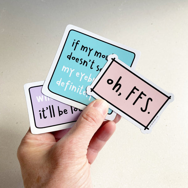 Hand holding three colorful stickers with humorous text on a plain background